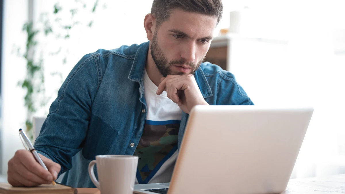 Man taking notes and looking at laptop screen